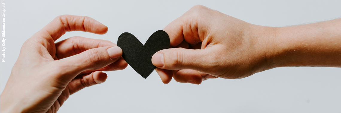 Two hands holding a black paper heart